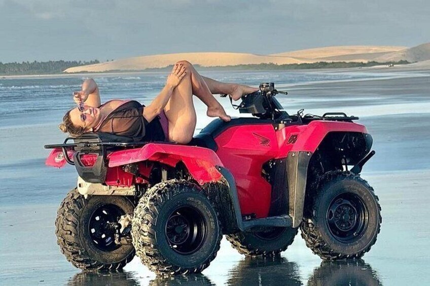 A person lying on a red ATV on a beach with water in the background. 2