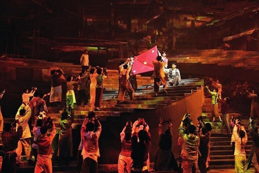 A group of people on a stage with a red flag, some standing and some sitting, in a dimly lit setting. 4