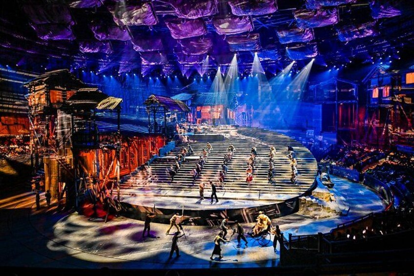 A stage with performers, a circular platform, and a large audience. 3