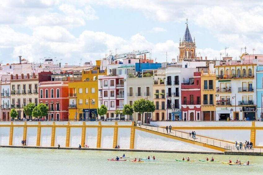 A waterfront promenade with colorful buildings, a bridge, and people kayaking. 1