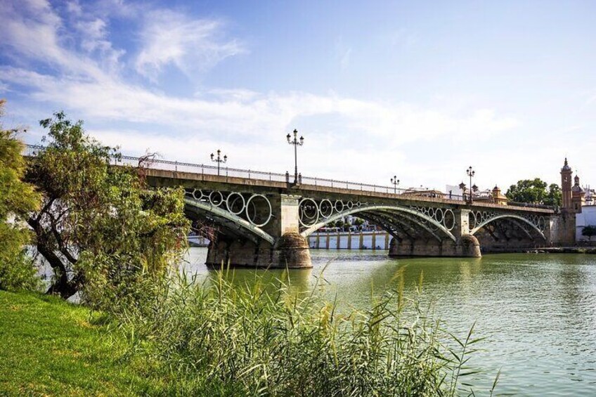 A stone bridge with circular designs over a river, surrounded by greenery and a clear sky. 5