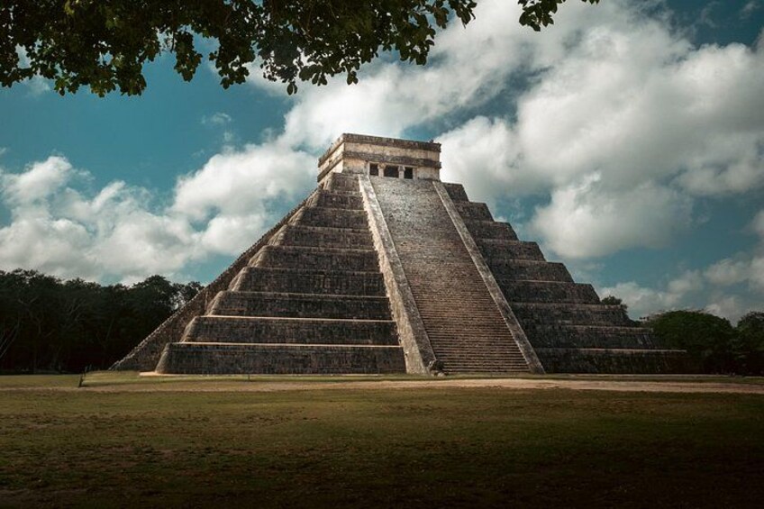 A large pyramid structure with multiple levels, surrounded by a grassy field and trees. 1