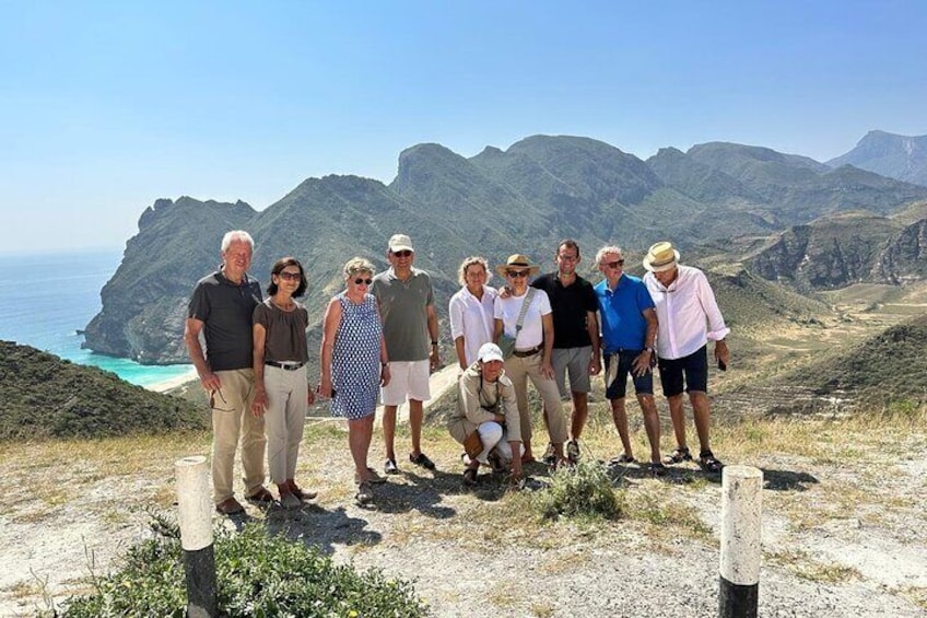 Un grupo de personas de pie en una ladera rocosa con vista al mar. 1