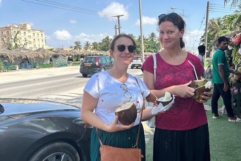 Dos personas sosteniendo cocos en una calle, con un coche y edificios al fondo. 3
