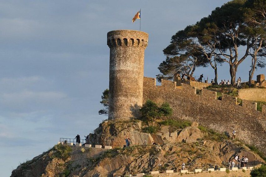 A stone tower with a flag, surrounded by a stone wall and trees. 2