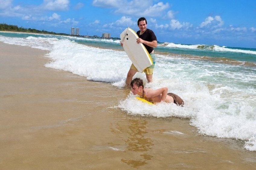 A beach with waves, a person lying on a yellow surfboard, and another person holding a white surfboard. 1