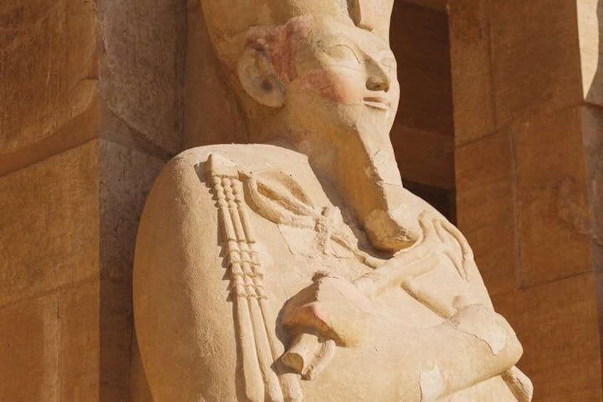 A stone statue of a seated figure with a crook and flail, a symbol of pharaonic power, set against a stone wall. 5