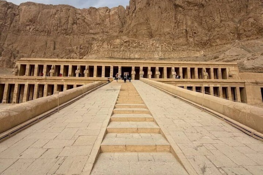 Une entrée monumentale, avec un long escalier menant à un temple, le tout entouré de falaises rocheuses. 2
