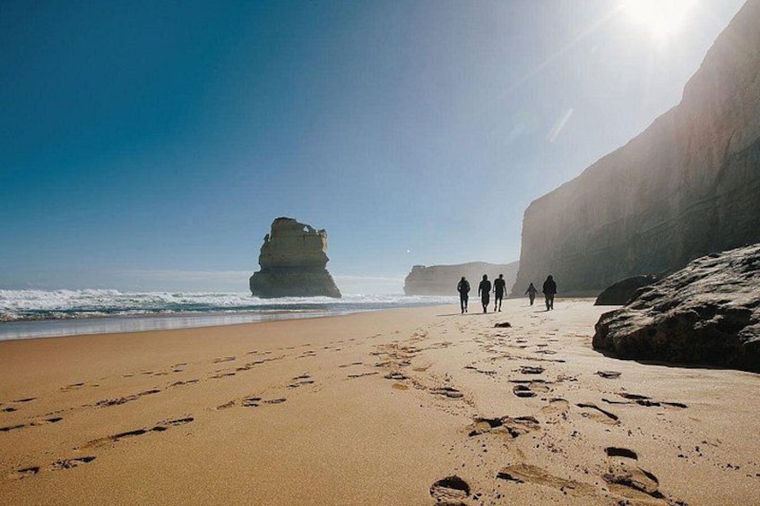 A beach with footprints leading to a rock formation, under a clear sky. 4