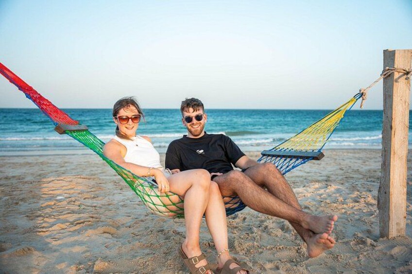 Zwei Personen entspannen in einer Hängematte an einem Sandstrand, im Hintergrund das Meer. 5
