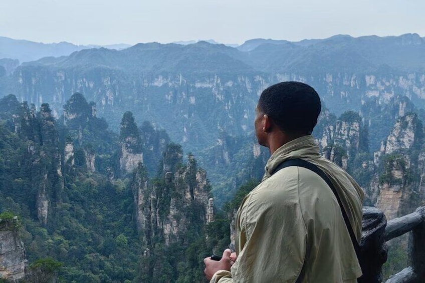 Une personne se tient au bord d’une falaise, surplombant une chaîne de montagnes boisées. 1