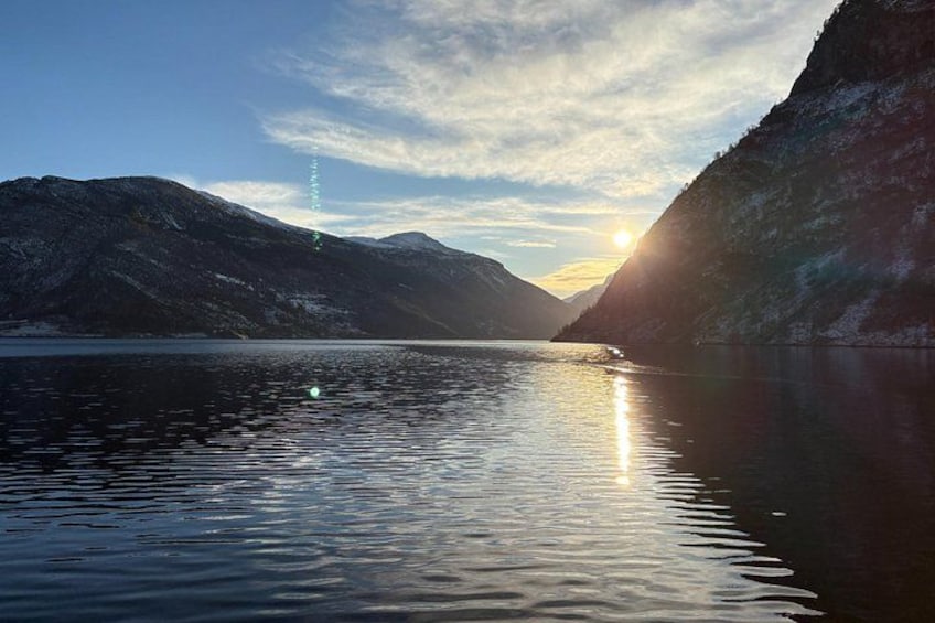 A calm lake with mountains in the background and the sun setting on the horizon. 2