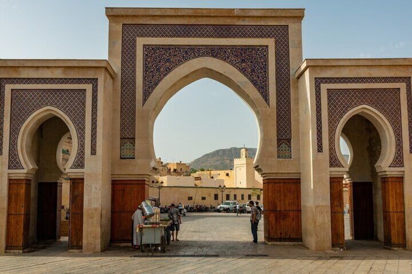 Un arco ornamentado con detalles en azulejos intrincados, que da acceso a un patio con un edificio al fondo. 2