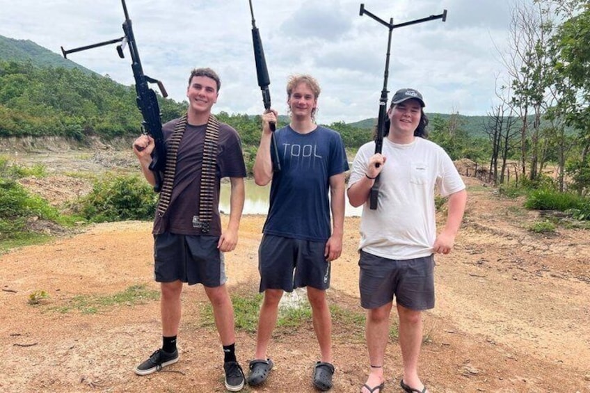Three individuals holding rifles in an outdoor setting with a dirt path and greenery in the background. 1