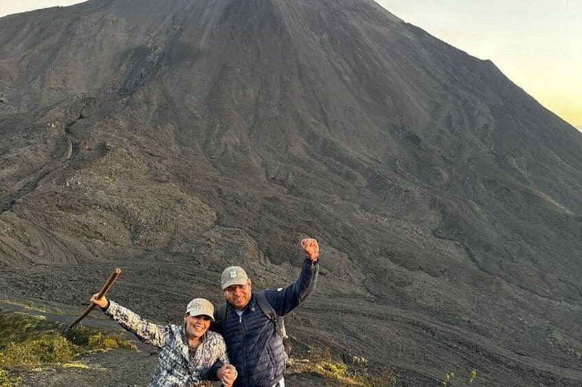 Two people standing in front of a large volcano. 4