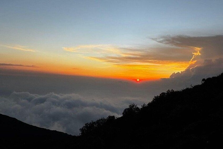 A sunset over a mountainous landscape with clouds below and a clear sky above. 2
