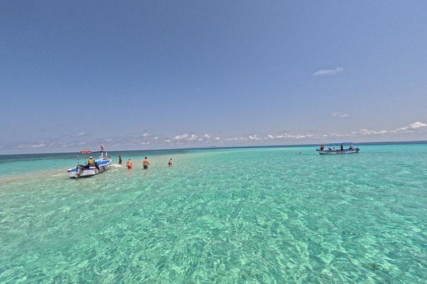 A clear turquoise sea with boats and people on the shore. 2