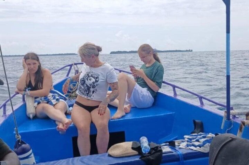 Drei Personen in einem Boot mit einer blauen Reling, im Hintergrund Wasser und eine entfernte Küste. 3