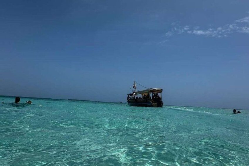 A boat on turquoise water, people swimming, and a clear sky. 3