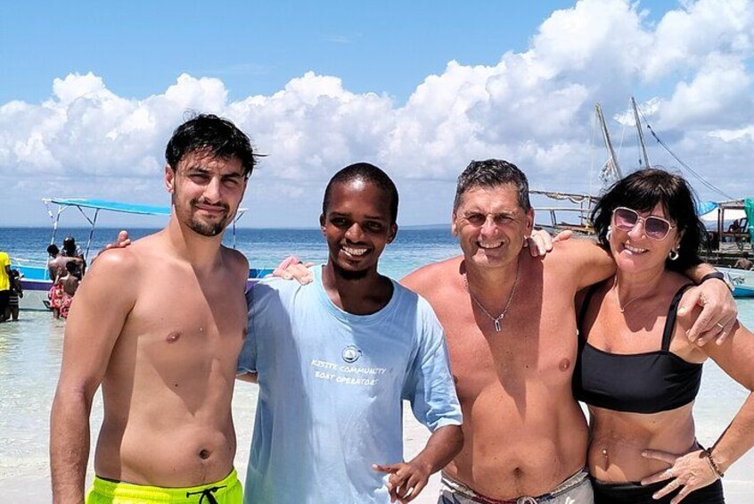 Eine Gruppe von Menschen am Strand, im Hintergrund Boote und Sonnenschirme. 2