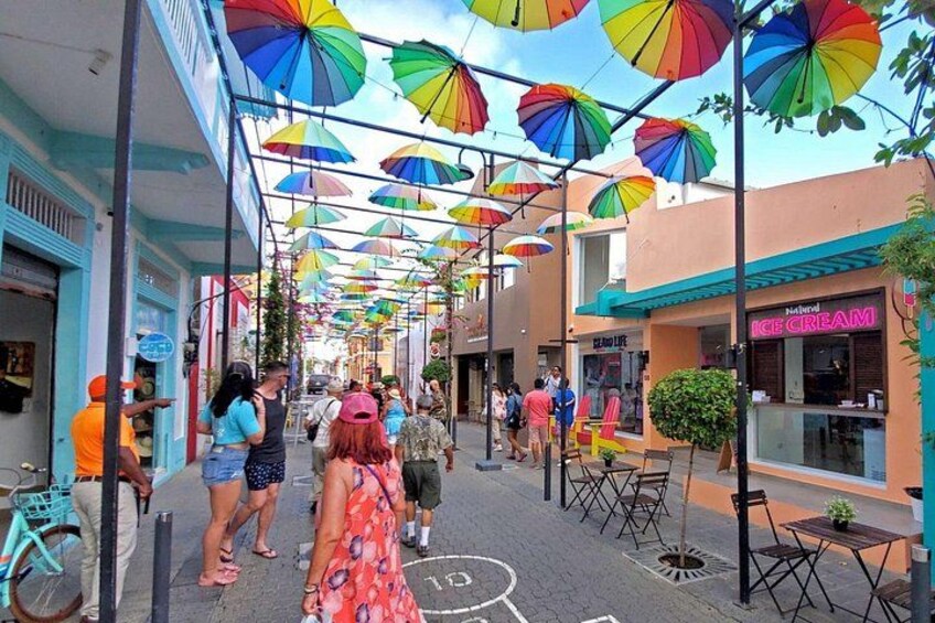 A street with colorful umbrellas, outdoor seating, and shops. 1