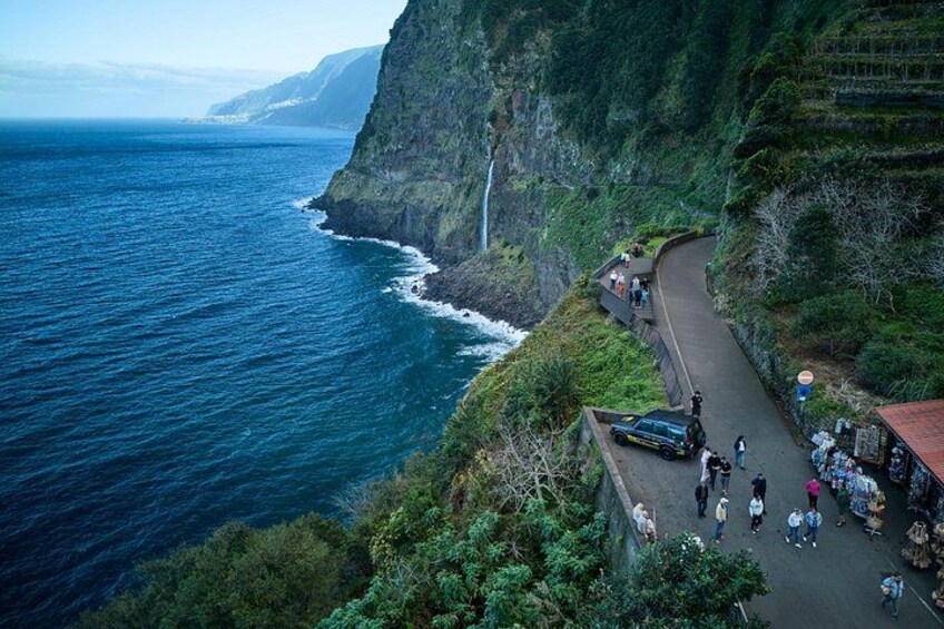A coastal road with a cliffside view, a waterfall, and a gathering of people. 3