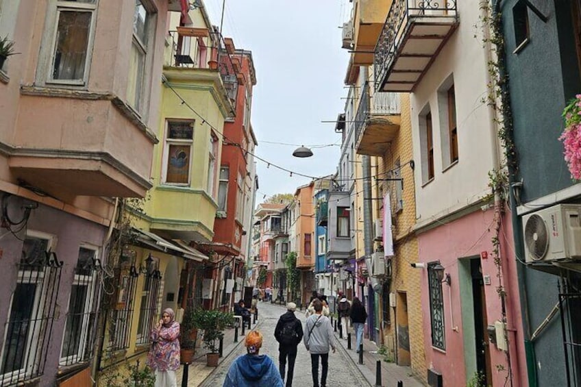 Una calle estrecha flanqueada por edificios coloridos, gente caminando y plantas colgantes. 4