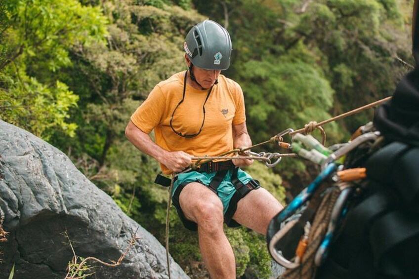Una persona con casco y camisa amarilla preparándose para descender en rápel por un acantilado rocoso. 5