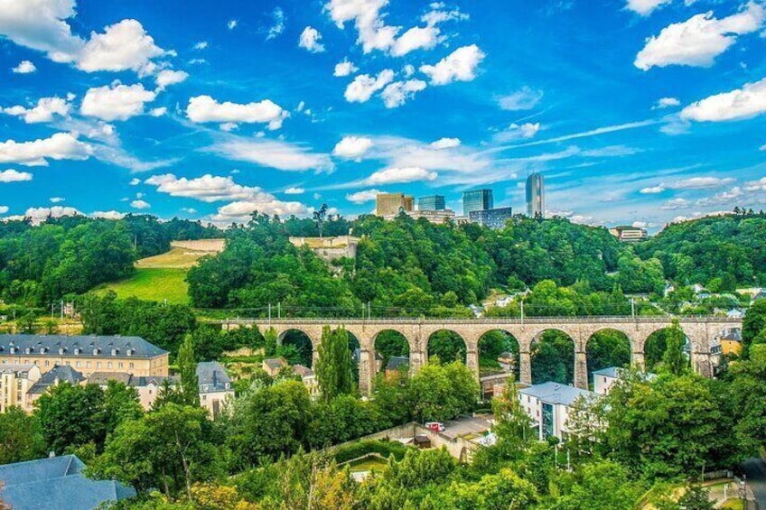 A stone aqueduct, lush greenery, and a cityscape with modern buildings in the background. 4