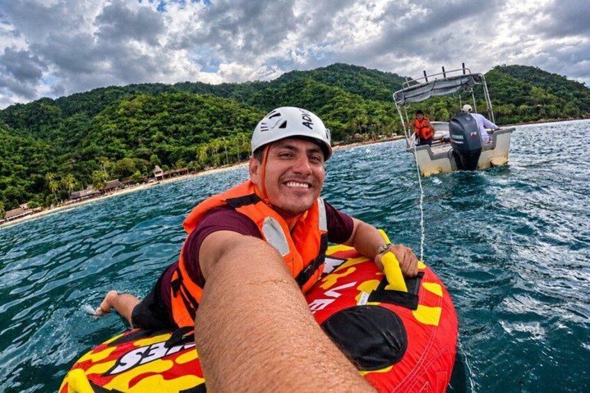 A person on a red and yellow inflatable raft in the water, with a boat and a mountainous landscape in the background. 5