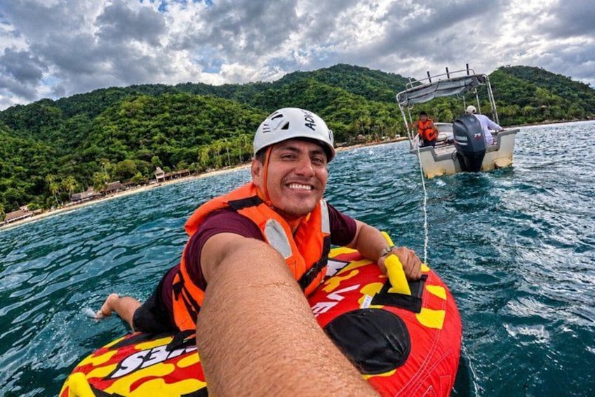 A person on a red and yellow inflatable raft in the water, with a boat and a mountainous landscape in the background. 3