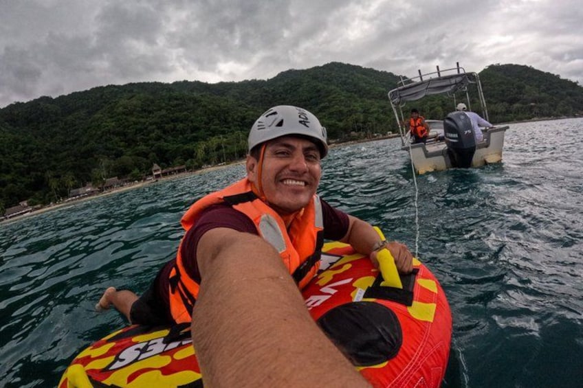 A person on a raft in a body of water with a boat in the background and a forested hill. 2