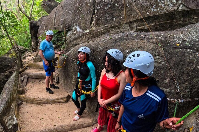 A group of people engaged in a rock climbing activity, wearing helmets and harnesses, on a rocky trail surrounded by trees. 2