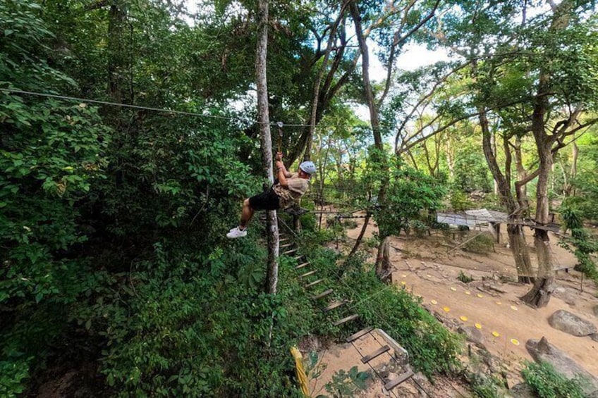 A person zip-lining through a forested area with dense foliage and a dirt path. 2