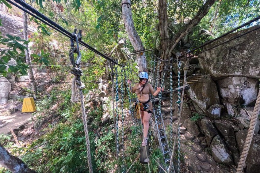A person on a rope course in a forested area with trees and rocky terrain. 3