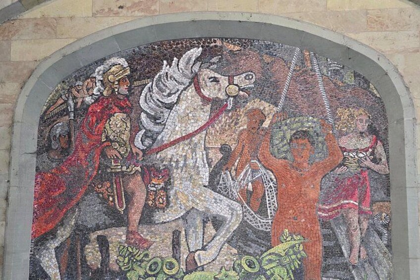 Une mosaïque représentant des personnages vêtus de costumes d’époque, intégrée à une structure en pierre en forme d’arc. 4