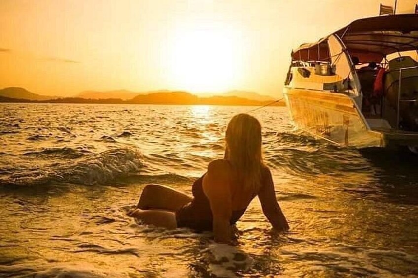 Eine Person sitzt im Wasser in der Nähe eines Bootes bei Sonnenuntergang. 1