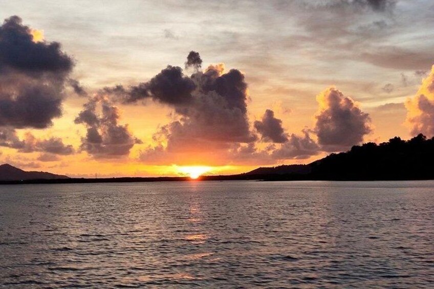 Ein Sonnenuntergang über einem Gewässer mit Wolken und der Silhouette einer Landmasse. 4