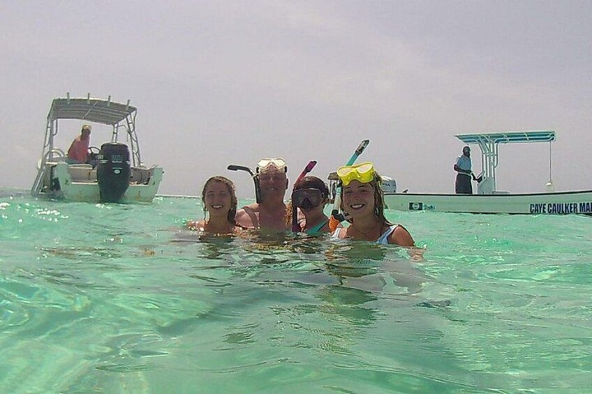 Personas en agua cristalina con un bote y un muelle al fondo. 2