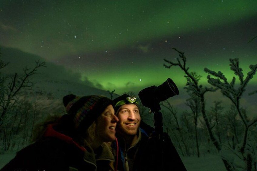Une personne, munie d’un télescope, se tient dans un paysage enneigé, sous une aurore boréale verdoyante. 1