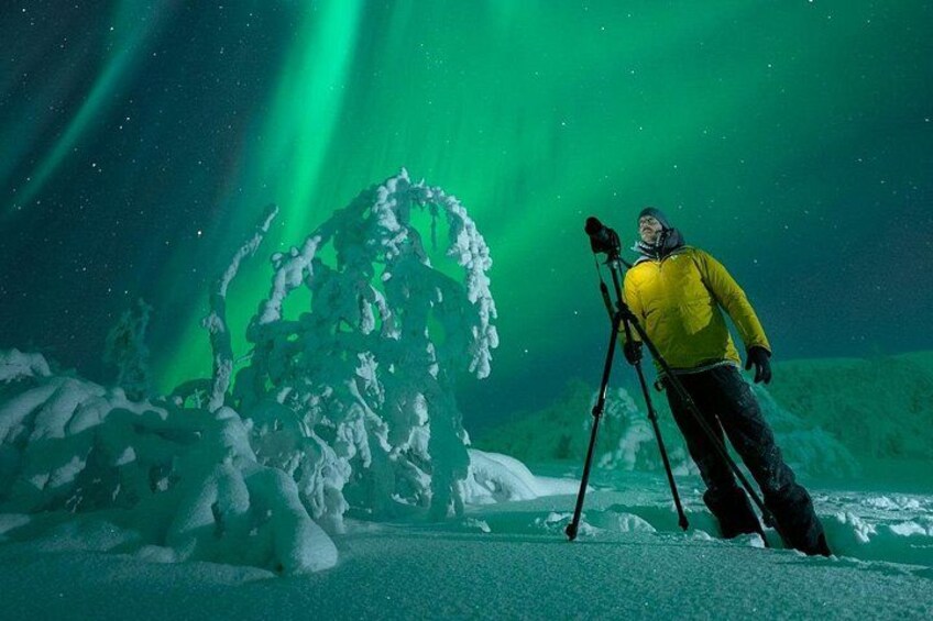 Une personne, appareil photo fixé sur un trépied, se tient sur un sol enneigé, avec une grande formation de glace en arrière-plan. 4