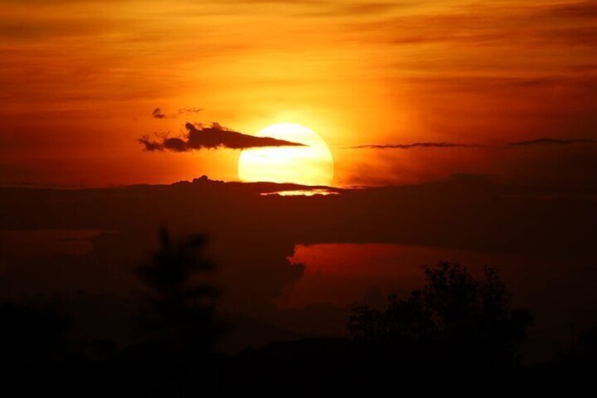 Un atardecer sobre una masa de agua, con siluetas de árboles y una cadena montañosa distante. 2