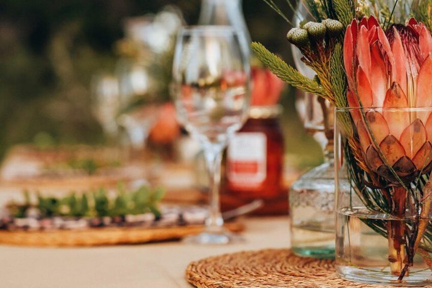 A table with a glass vase containing a red flower arrangement, a bottle, and a glass of water. 4