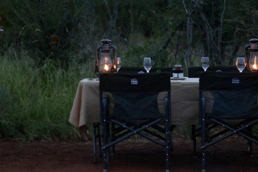 A camping table set up outdoors with chairs, a tablecloth, and lanterns. 2