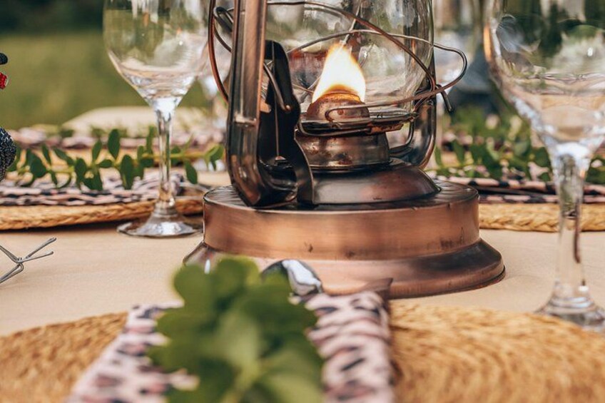 A copper lantern with a lit candle, surrounded by wine glasses and a woven placemat. 3