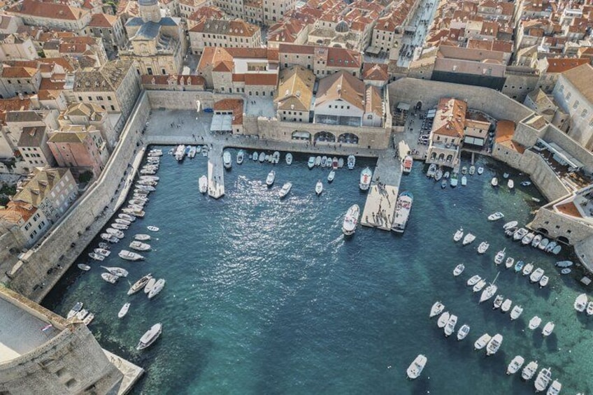 An aerial view of a historic harbor with numerous boats docked along the waterfront, surrounded by old buildings and fortifications. 2