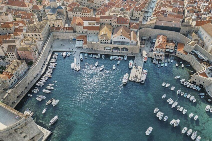 Ein Hafen mit zahlreichen vor Anker liegenden Booten, umgeben von historischen Gebäuden und einer markanten, festungsähnlichen Struktur. 2