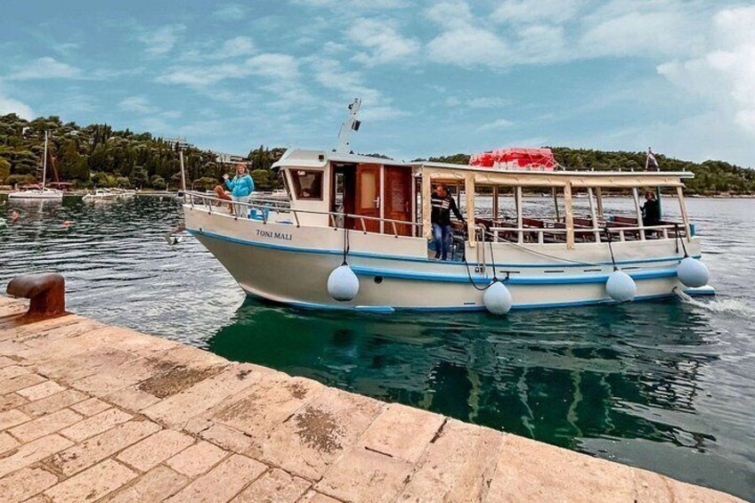 Ein Boot namens 'TONI MALI' liegt an einem Steg im ruhigen Wasser unter blauem Himmel. 5