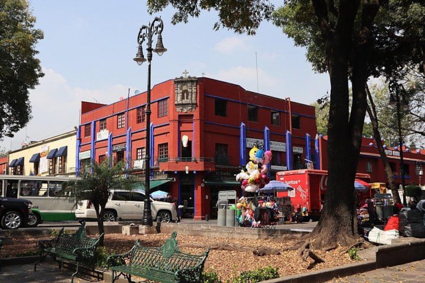 A red building with blue accents, a parked car, a bus, and a tree in the foreground. 3