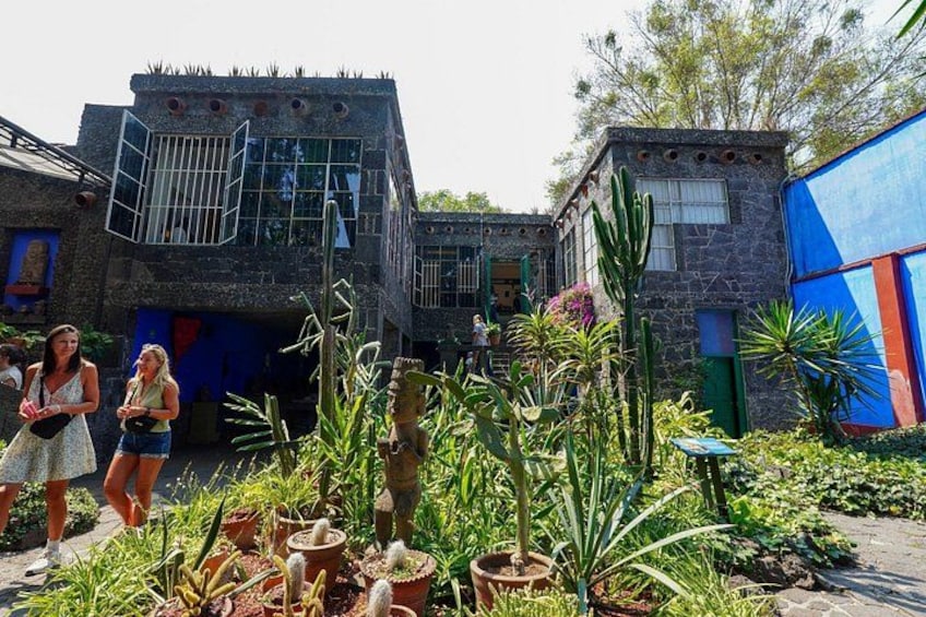 A courtyard with cacti, a stone building, and a blue structure. 1